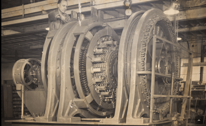 A worker inspects a large mechanical generator within a factory, showcasing industrial innovation and engineering expertise.